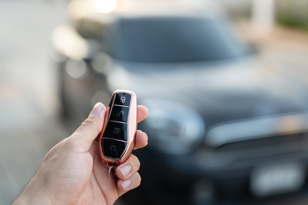 Hand holding a modern car key fob with buttons for locking and unlocking, blurred vehicle in background, illustrating key fob programming and ignition services offered by Swift Locksmith in Raleigh, NC.
